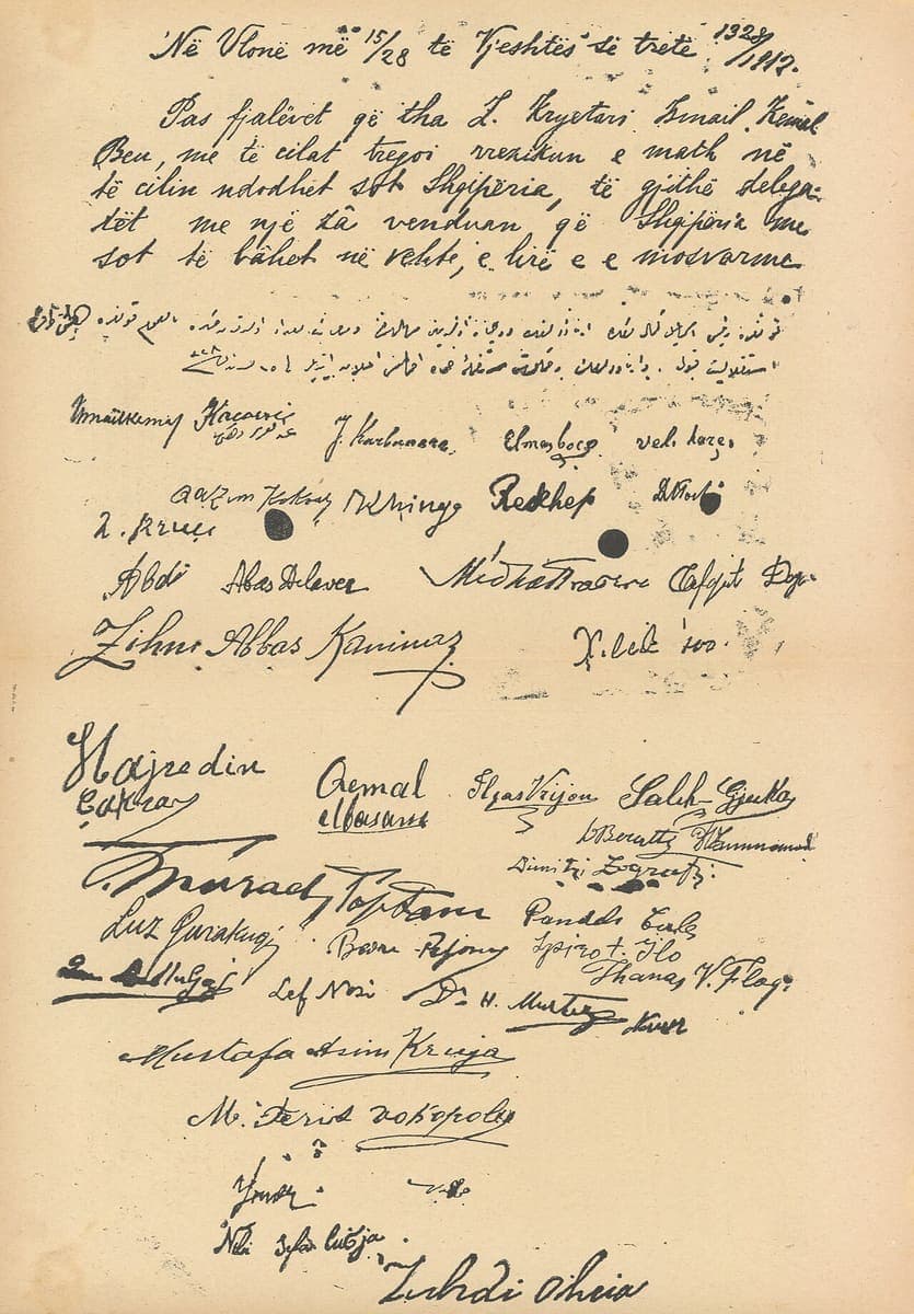 Handwritten page with Albanian Latin-script paragraphs at the top, two lines of Arabic-script Ottoman Turkish below, and dozens of signatures in Latin and Arabic script filling the rest of the page