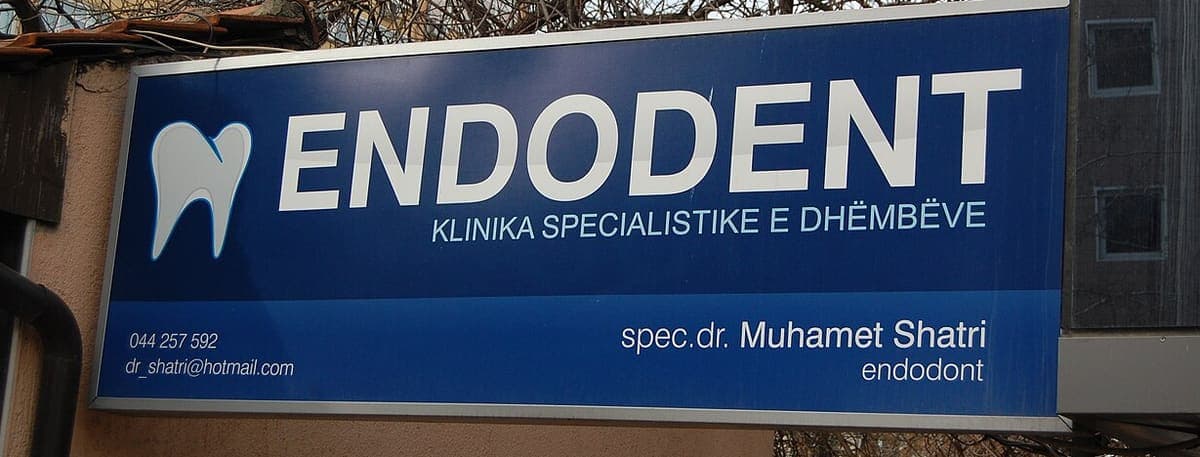 Blue backlit clinic sign reading Endodent, Klinika Specialistike e Dhëmbëve, with a phone number and the specialist’s name