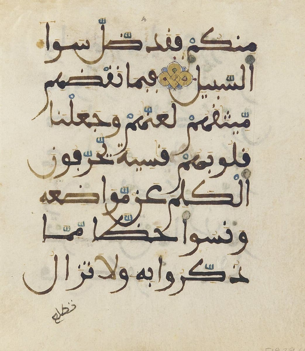 Parchment folio with seven lines of brown Maghribi script, gold vowel marks and blue reading marks, a gold verse rosette and a catchword at the foot