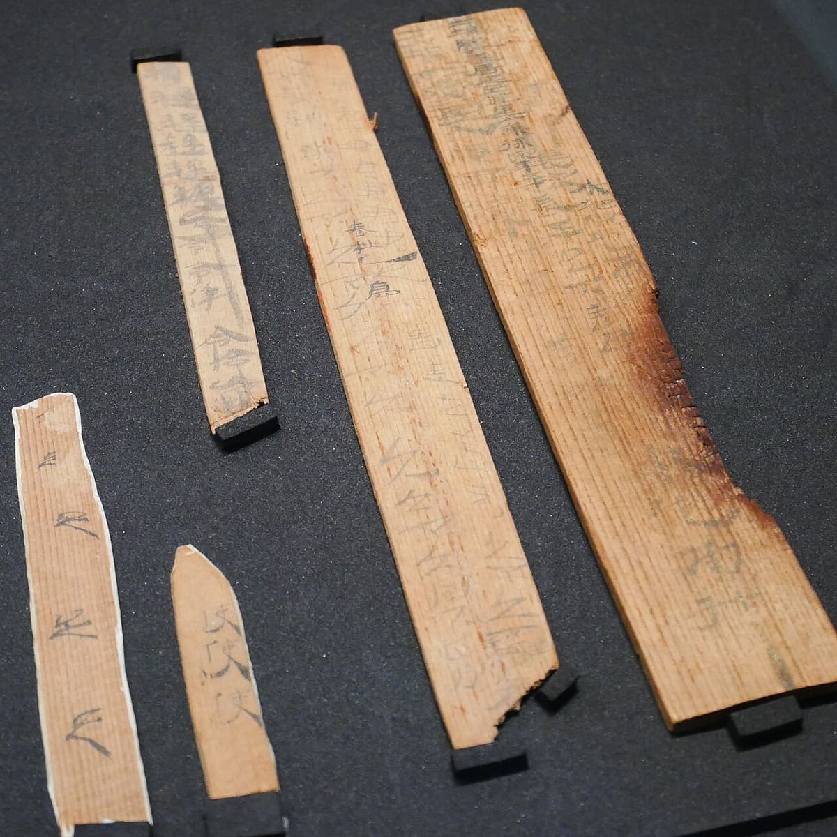 Five Han wooden slips and boards of different widths, covered with repeated characters in a quick brushed clerical hand
