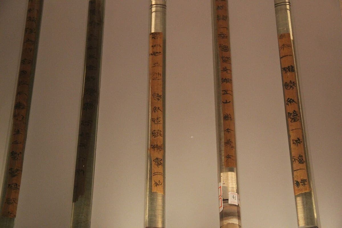 Close view of five Warring States bamboo slips in glass mounts, each with a single column of brush-written graphs in dark ink