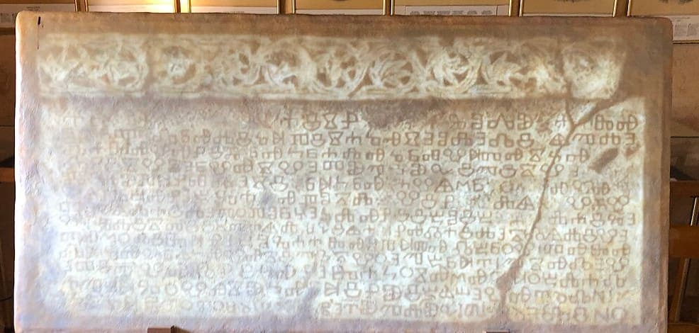 Cropped photograph of the Baška tablet, a stone slab carved with an interlace border above rows of angular Glagolitic letters