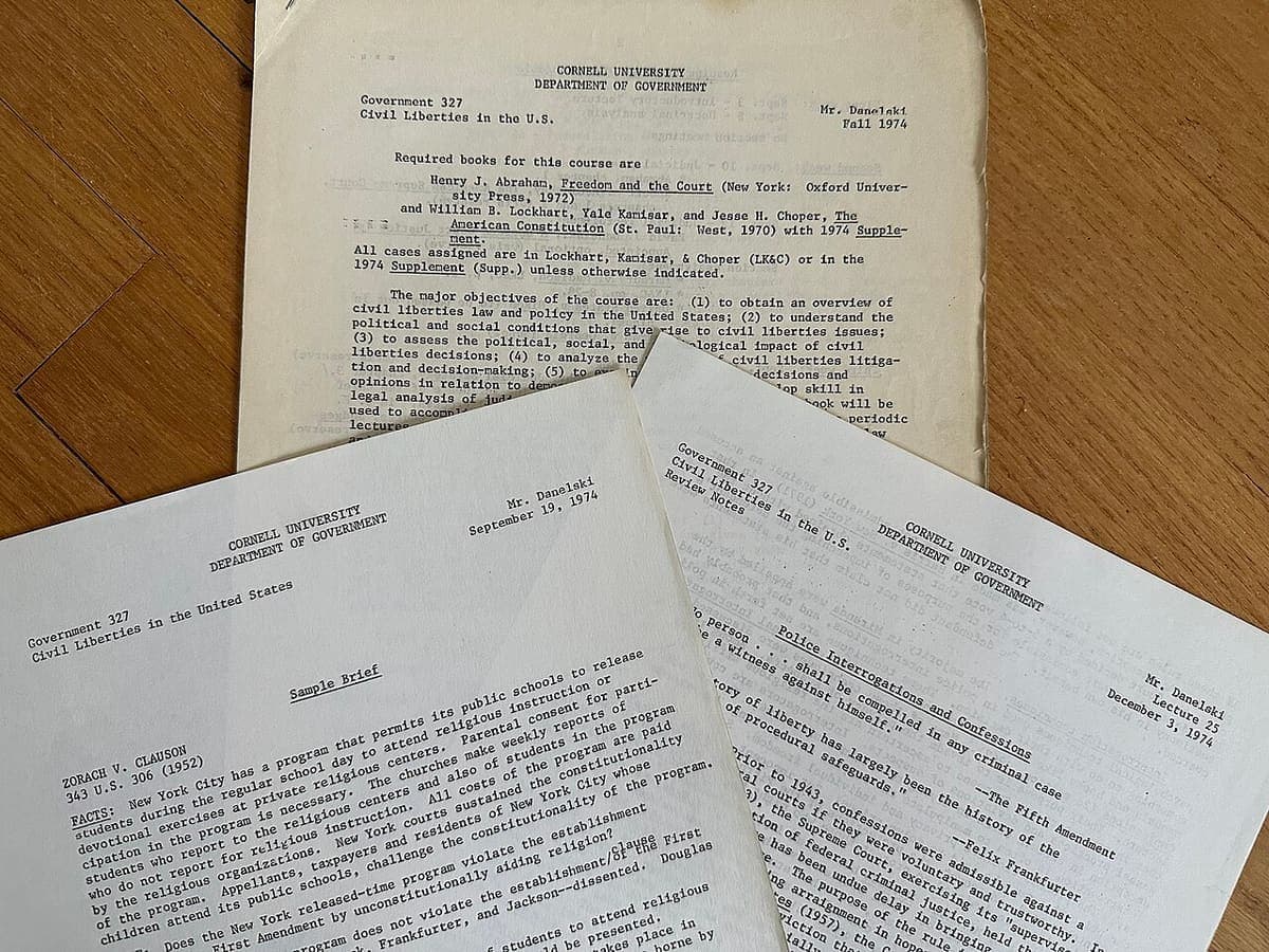 Three typed course handouts lying overlapped on a wooden table, photographed at an angle so each partly covers the next