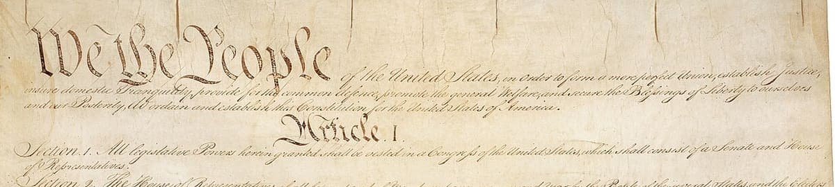 The head of a large parchment sheet with We the People in black letter followed by long ruled lines of engrossed script