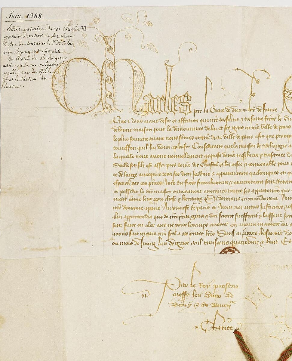 The left-hand part of a parchment charter: the king’s name in tall decorated letters, lines of fine brown chancery cursive below it, a later archivist’s note in the corner and a folded lower edge carrying a subscription
