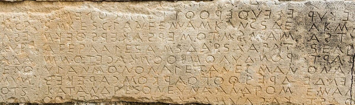 Close-up of the Gortyn law code wall in Crete with eight lines of large boustrophedon Greek letters cut into limestone blocks