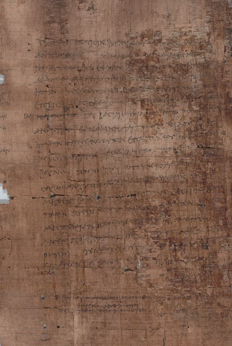 Brown papyrus with about twenty lines of small faded Greek cursive and, below a blank space, two larger lines in a different hand