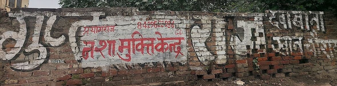 Whitewashed brick wall in Prayagraj painted with large Devanagari letters in white and red, with a telephone number