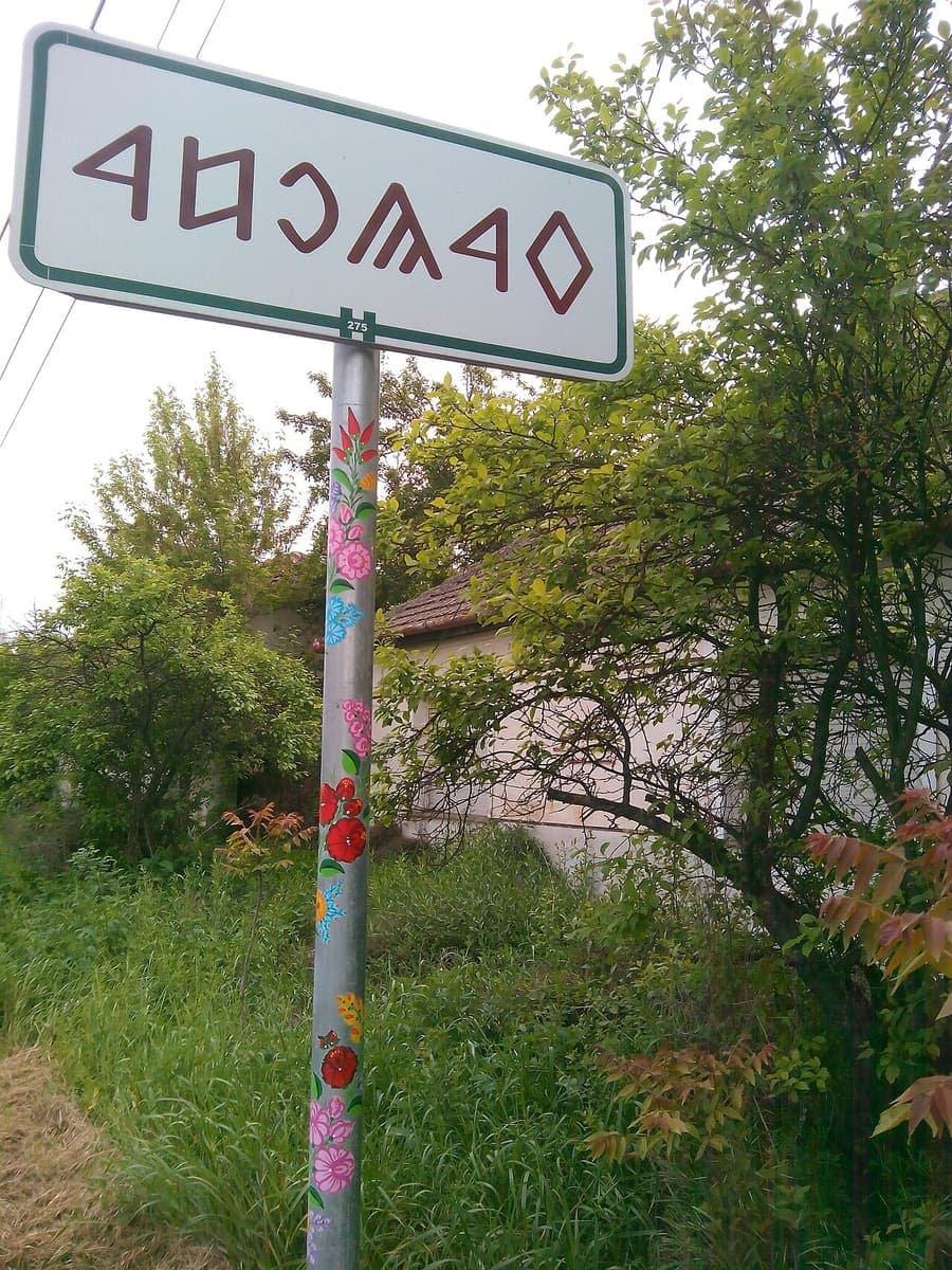 Town-limit road sign for Kalocsa written in Old Hungarian runic letters on a post painted with folk-art flowers