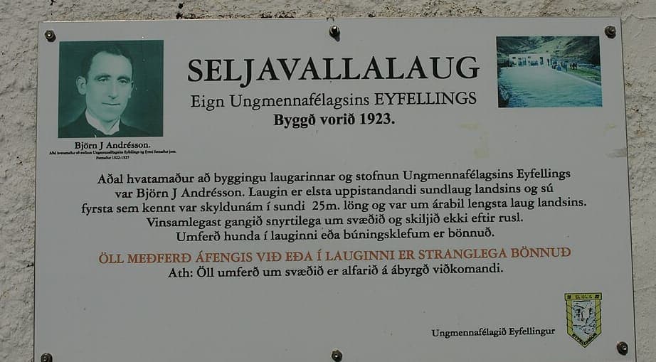 Weathered metal plaque on a cracked wall headed SELJAVALLALAUG, with a photograph of a man and seven lines of Icelandic text below, one line printed in red