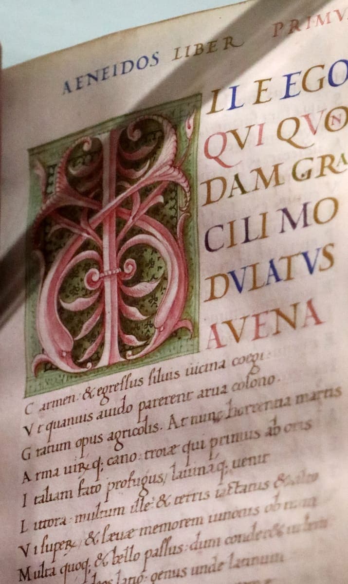 Opening page of the Aeneid in a Renaissance codex: six display lines in coloured capitals beside a white-vine initial, then verses in a fine sloping humanistic hand
