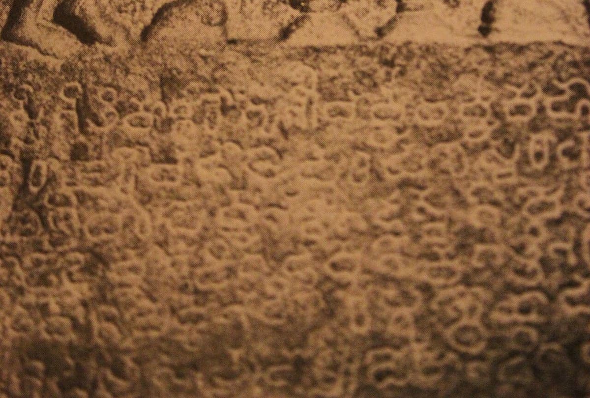 A close view of a weathered stone memorial filled with lines of Old Kannada inscription, worn carving showing along the top edge