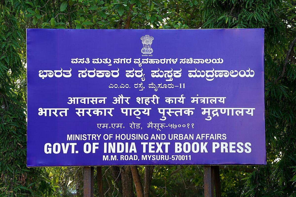 A blue government signboard giving the same institution name in Kannada, Hindi and English beneath the national emblem