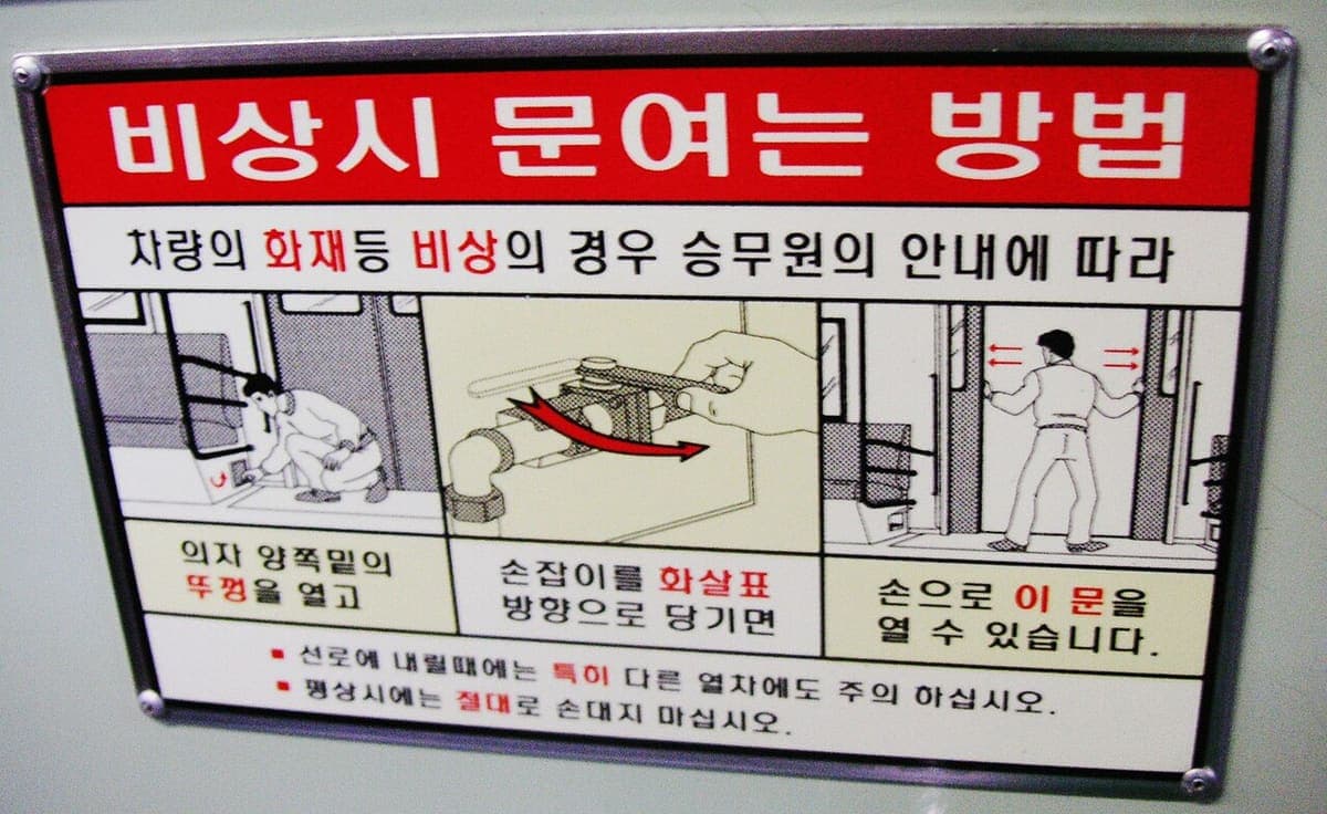 Enamelled instruction plate inside a Seoul metro carriage, horizontal hangul in red and black over three captioned drawings
