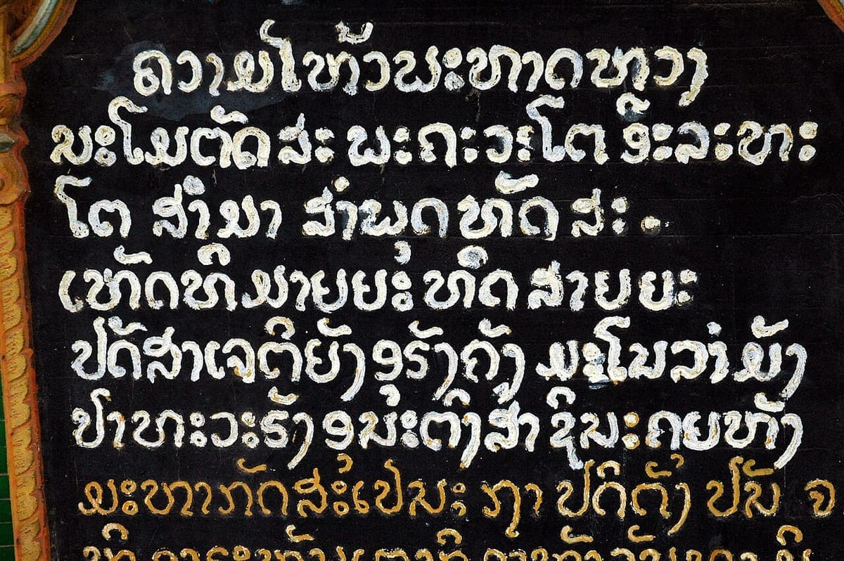 Black lacquered temple signboard at Wat That Luang, Vientiane, with several lines of Lao script painted in gold and white