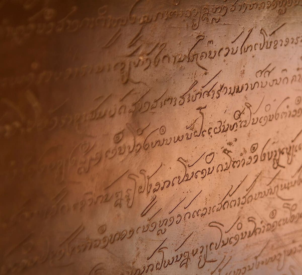 Close view of an inscription cut into a smooth brown surface, ten or so cursive lines of old Lao script running diagonally under raking light