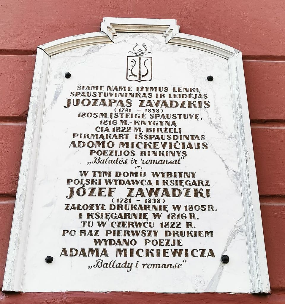 White marble memorial plaque with matching Lithuanian and Polish inscriptions naming the printer Juozapas Zavadskis and the 1822 first printing of Mickiewicz’s poetry