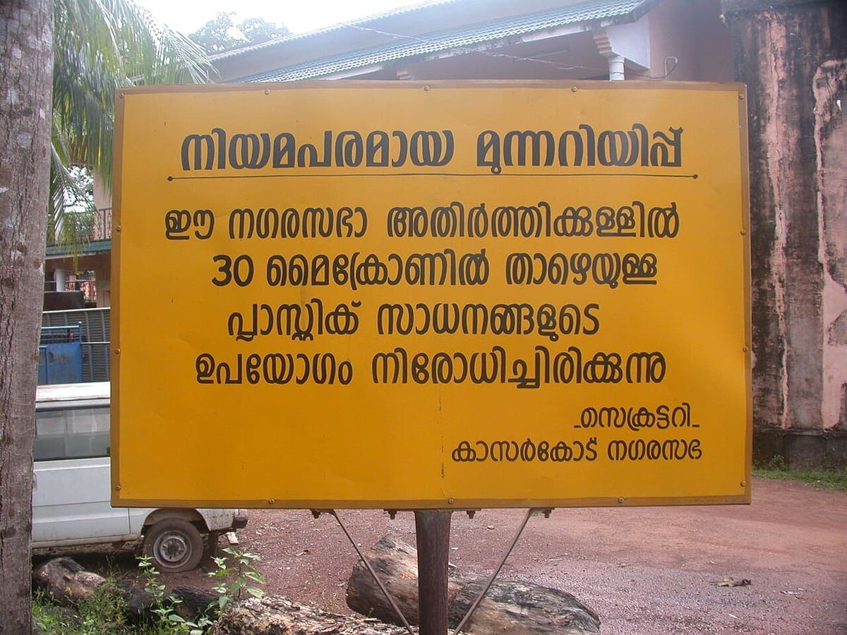 A yellow municipal notice board in Malayalam banning thin plastic items, signed by the Kasaragod municipality secretary