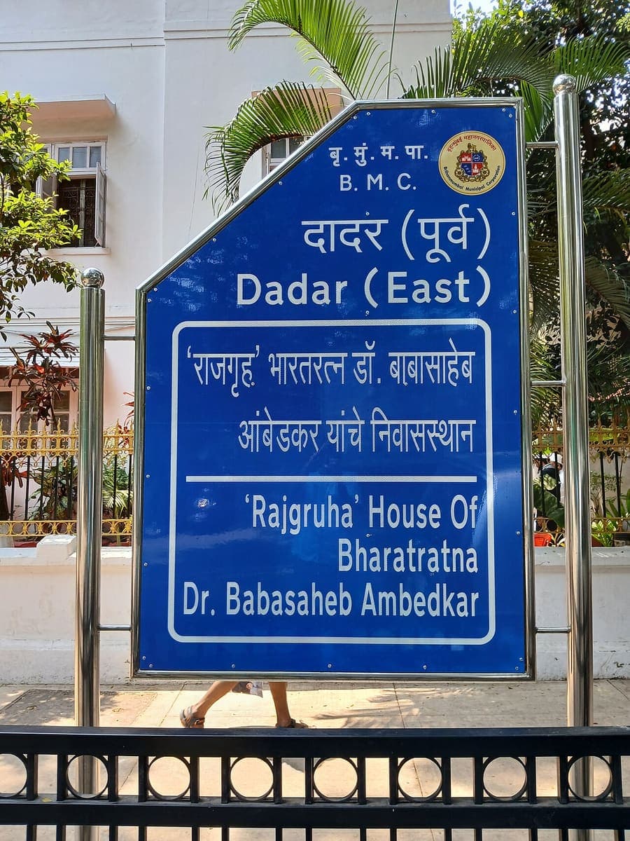 A blue municipal signboard outside a house, giving the address and the building name in Devanagari and English one above the other