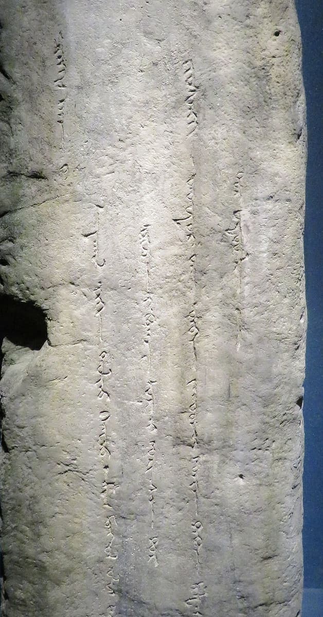 Five vertical columns of lightly incised Mongolian script running down the pitted, pale granite face of a tall stele standing in a museum case