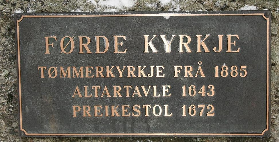 Bronze plaque on a snow-capped stone gatepost reading Førde kyrkje with three dated building details below