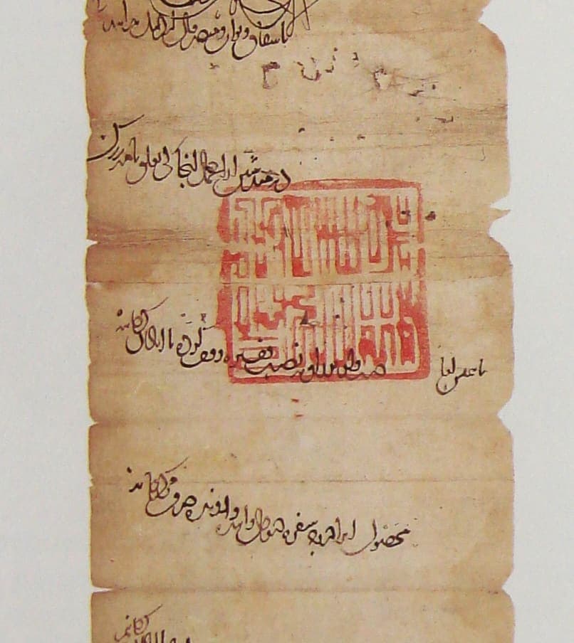 Section of a narrow paper scroll with widely spaced sloping lines of Persian and a square red seal stamped across the middle