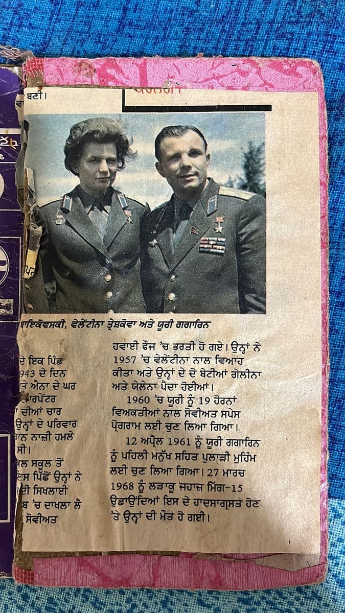 A torn and foxed Punjabi newspaper clipping pasted into a scrapbook, with a colour photograph of two Soviet cosmonauts above two columns of Gurmukhi print