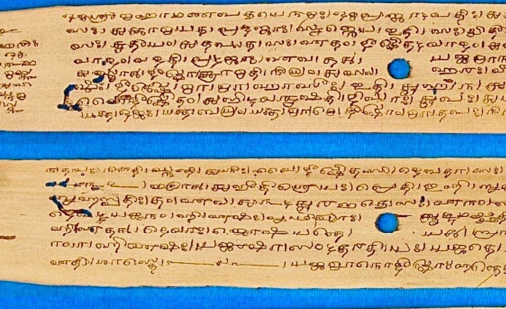 Two long strips of palm leaf laid on a blue ground, each incised with seven or eight dense lines of rounded Grantha writing