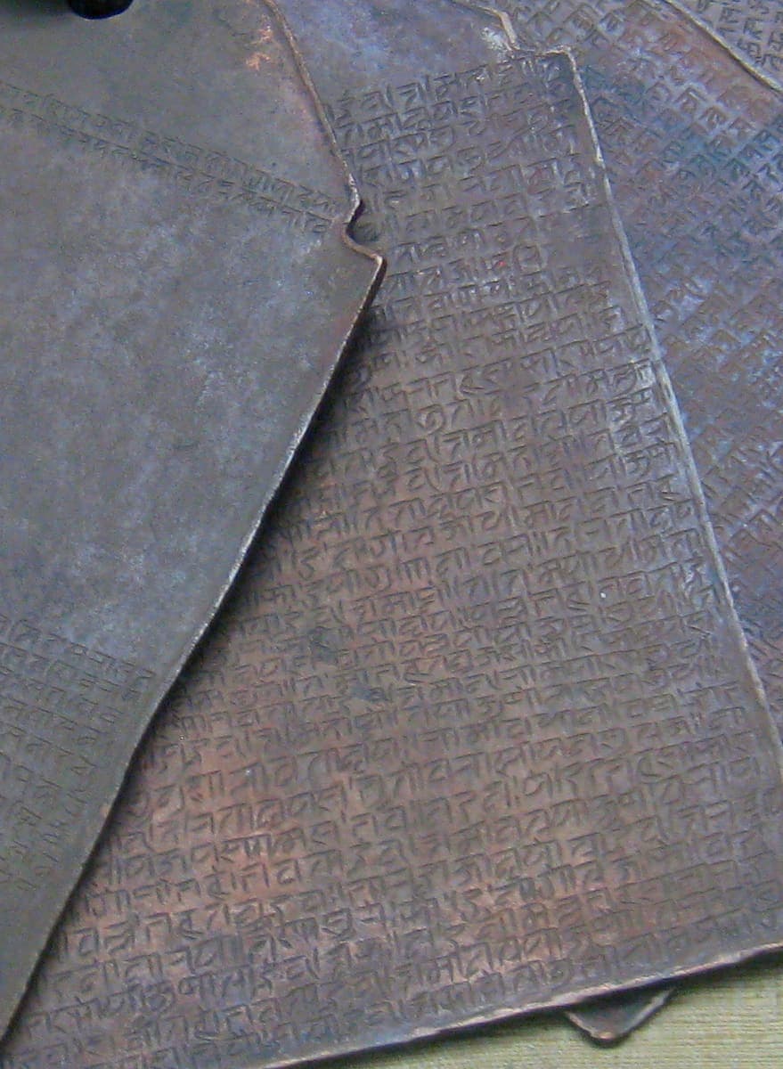 Overlapping sheets of dark copper engraved with close rows of letters, fanned out around a ring