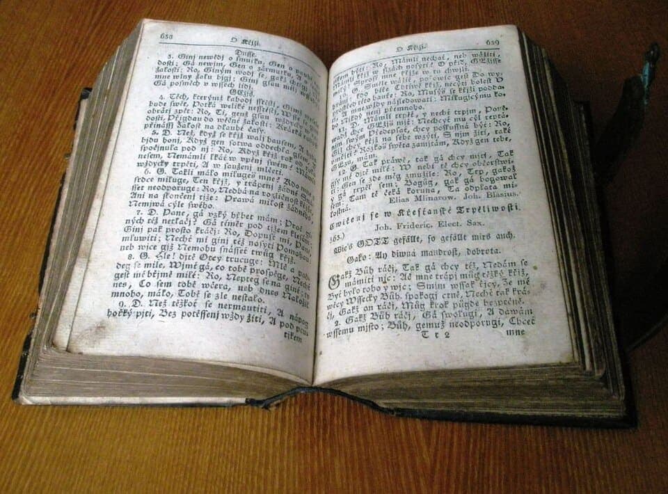 Open early nineteenth-century hymnal photographed on a table, two facing pages of dense black-letter-adjacent type in older Czech orthography