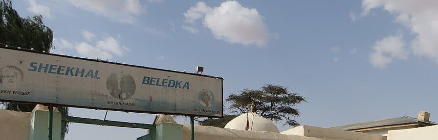 A white sign reading SHEEKHAL BELEDKA mounted above a green-painted gateway, with small portrait roundels labelled with sheikhs' names