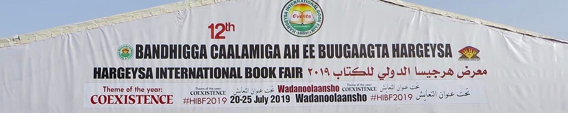 A wide banner spanning a book-fair entrance, its bold Somali headline followed by English and Arabic translations below