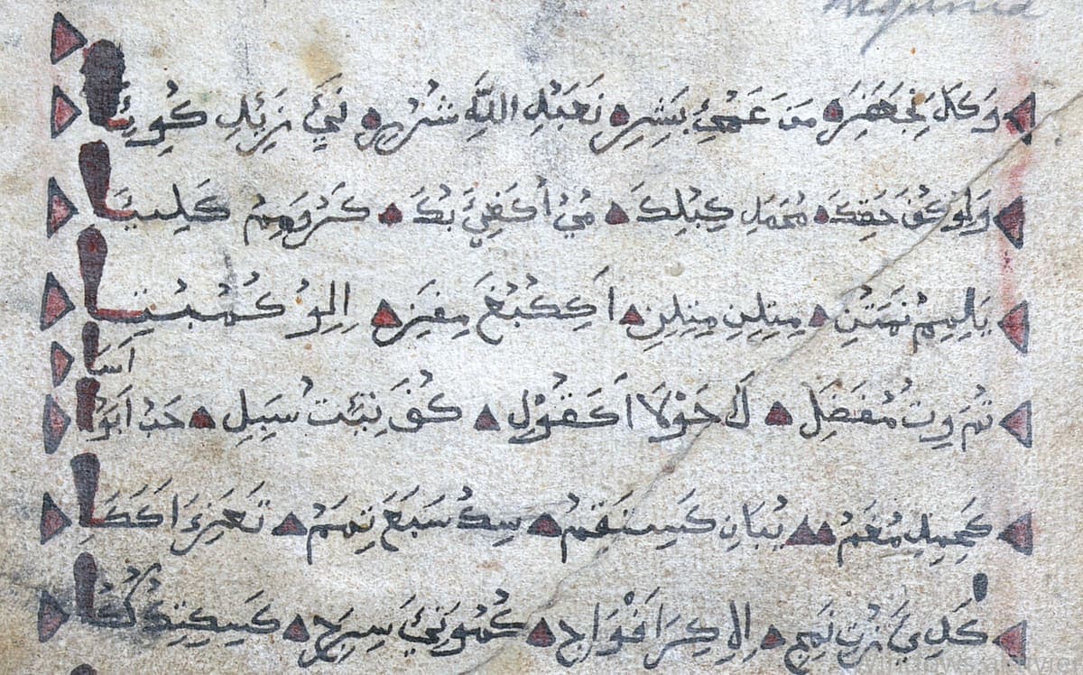 A worn paper manuscript page of Arabic-script verse in black ink, with small red and black triangular marks after each line