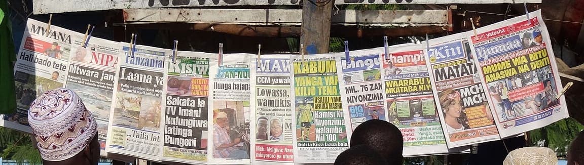 A row of Swahili-language newspaper front pages clipped to a line at a roadside newsstand