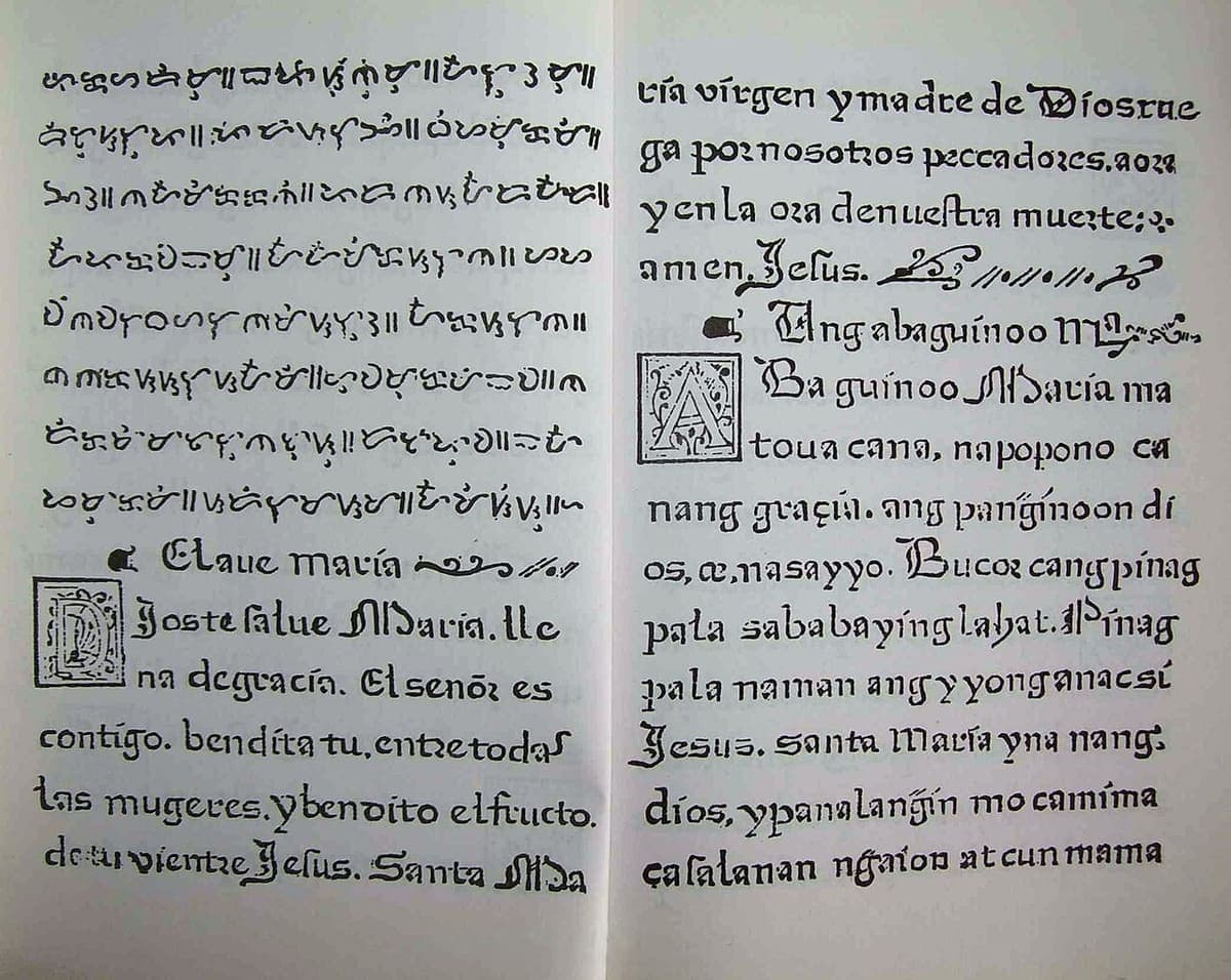 An opening of a 1593 book with eight lines of baybayin syllabic script at the head of the left page, the Spanish prayer in Gothic type below it, and the romanised Tagalog version on the right page