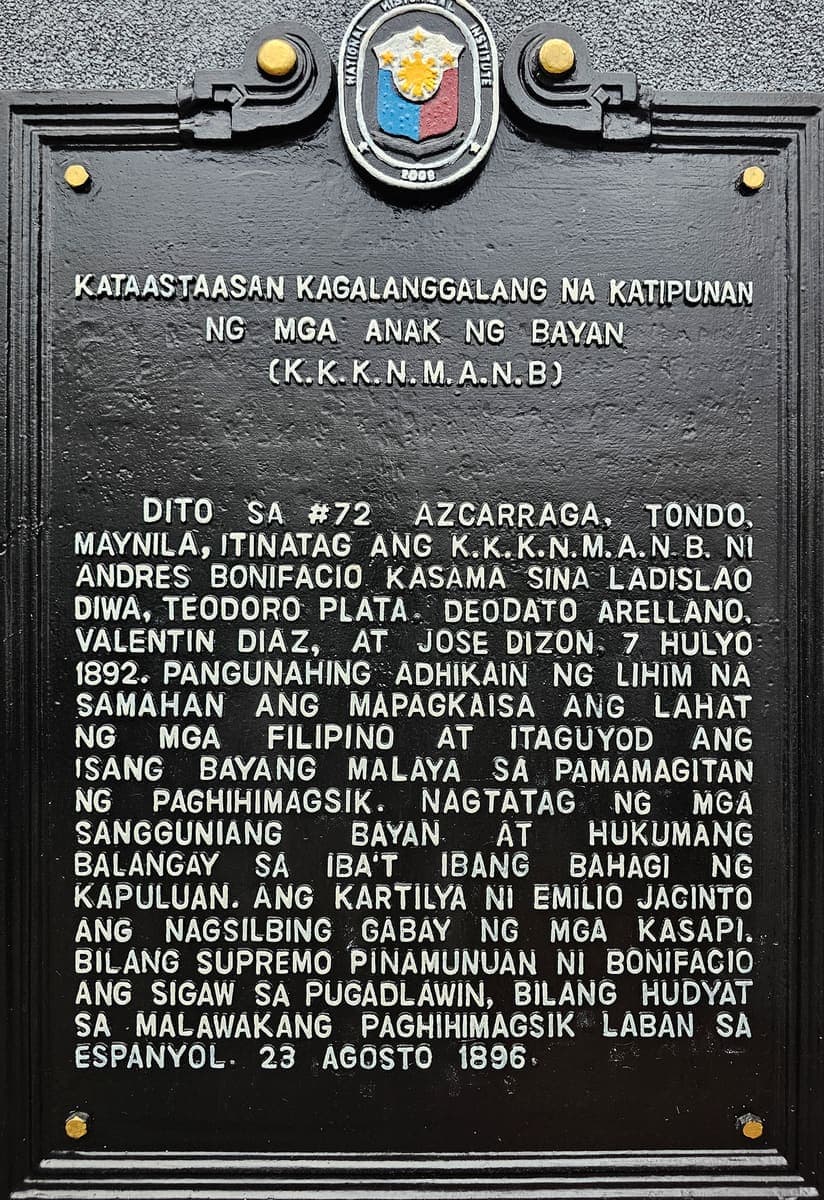 A black cast-metal historical marker with raised capital letters in Filipino, topped by the oval seal of the National Historical Institute