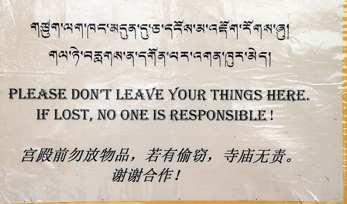 Laminated trilingual notice with two lines of printed dbu-can Tibetan at the top, English in a decorative typeface in the middle, and Chinese characters below