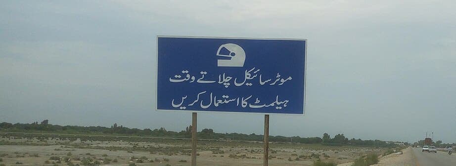 Blue Pakistani highway sign with two lines of printed Urdu telling motorcyclists to wear a helmet