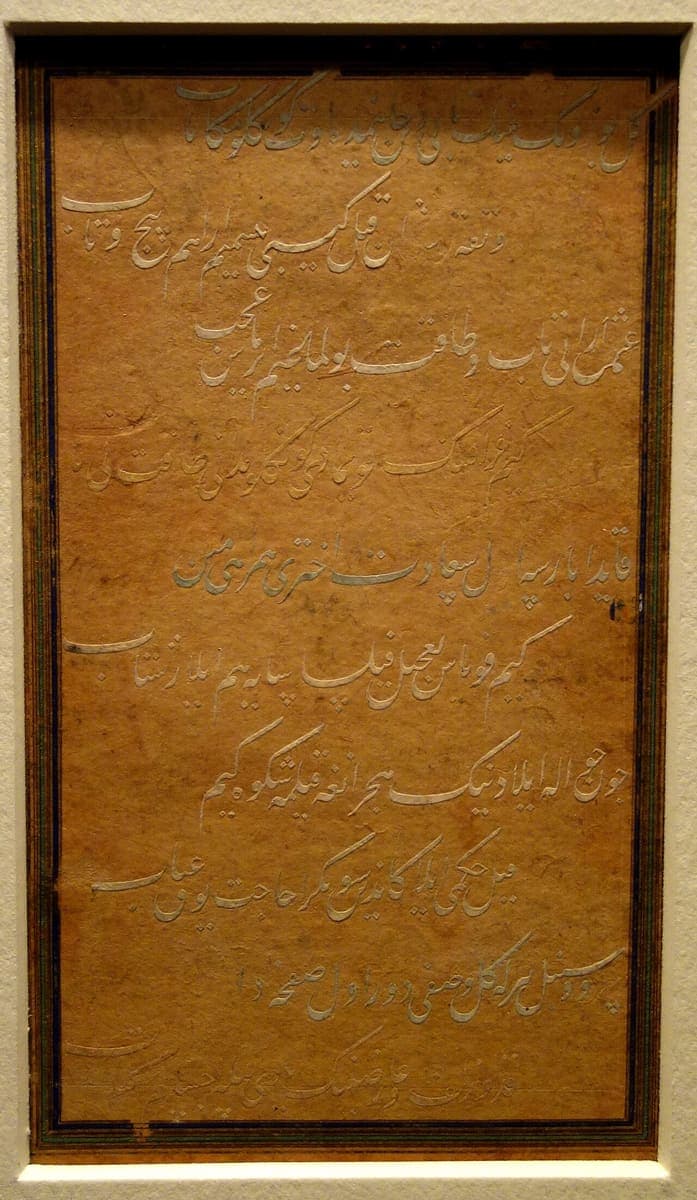 A framed album folio of gold and silver Nastaliq calligraphy on tan paper, ten lines of flowing Chagatai Turkish verse under museum glass