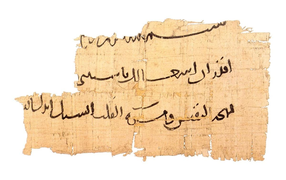 Torn papyrus with three lines of large, confident Arabic writing in dark ink, a few letters carrying dots