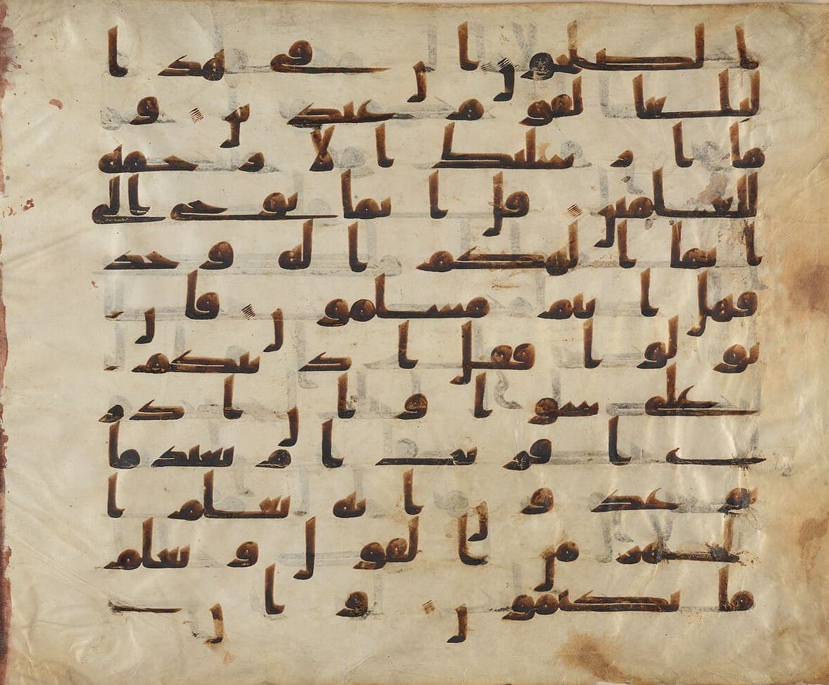 Very large parchment leaf with nine lines of massive angular Kufic letters in brown ink, ruled lines faintly visible behind them