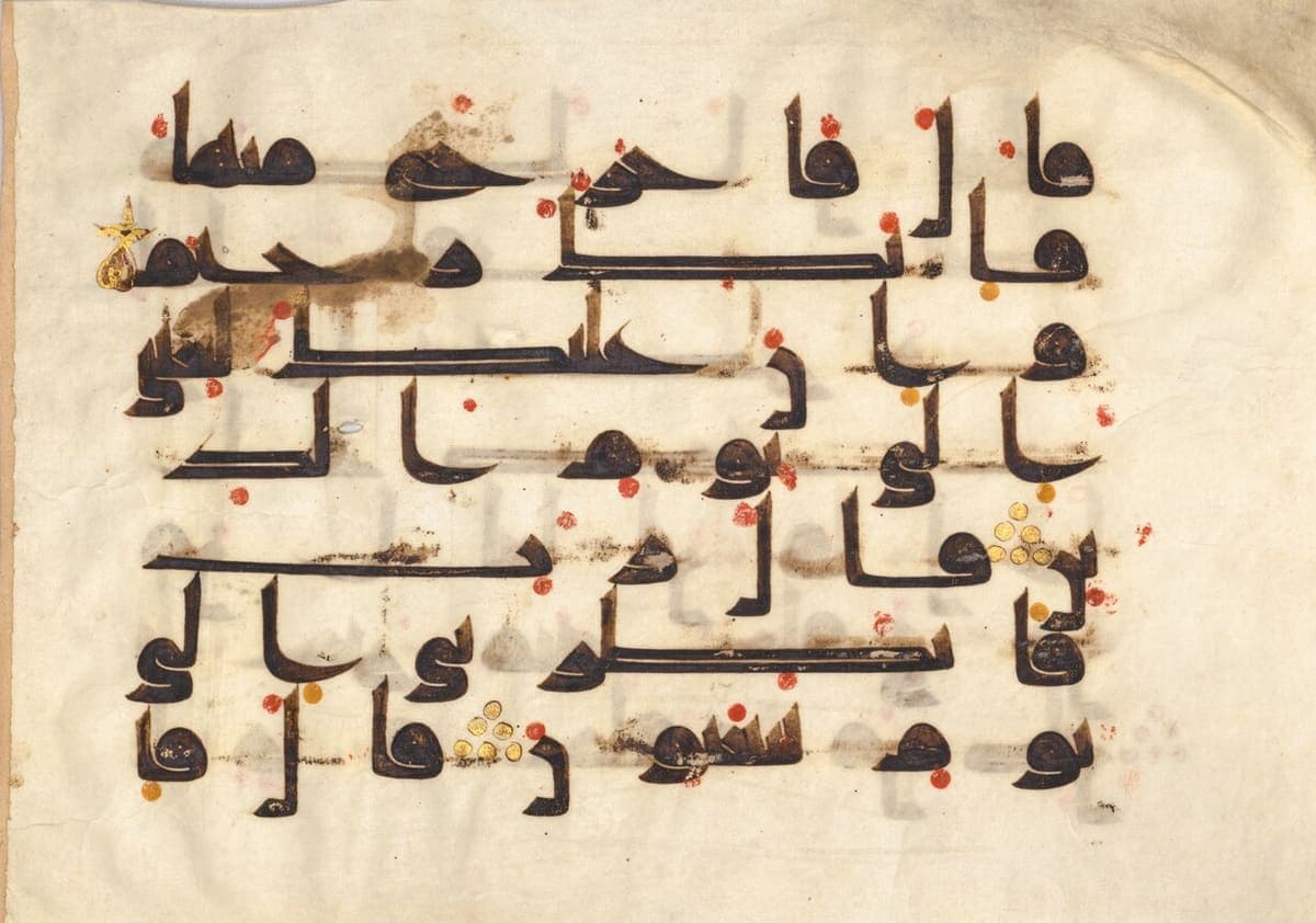 Wide parchment folio with seven lines of heavy Kufic script, scattered red dots above and below the letters and small gold discs between words