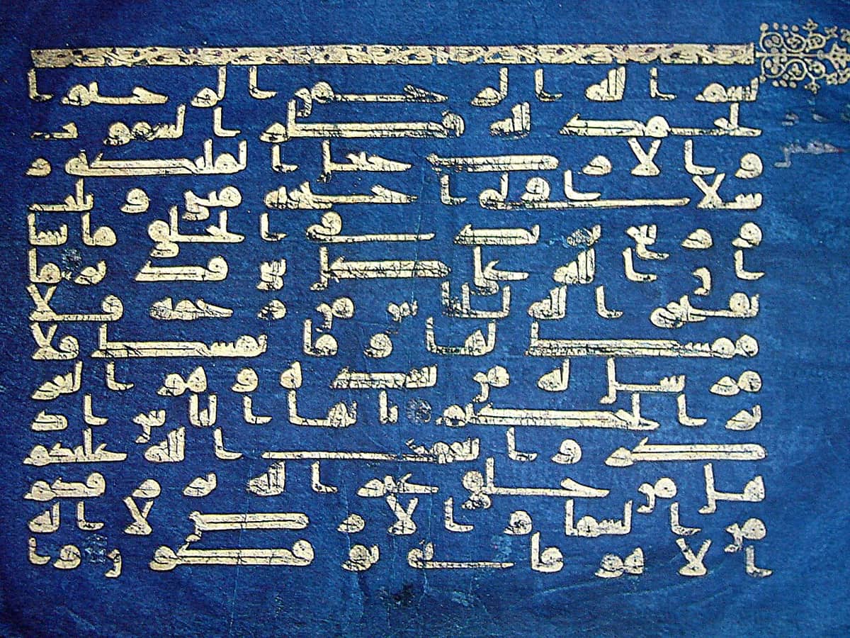 Indigo-dyed parchment carrying fourteen lines of gold Kufic script under an ornamented gold band across the top of the page