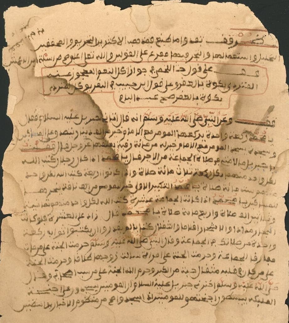 Water-stained paper leaf of a West African manuscript, with red headings, a boxed passage and small glosses down both margins