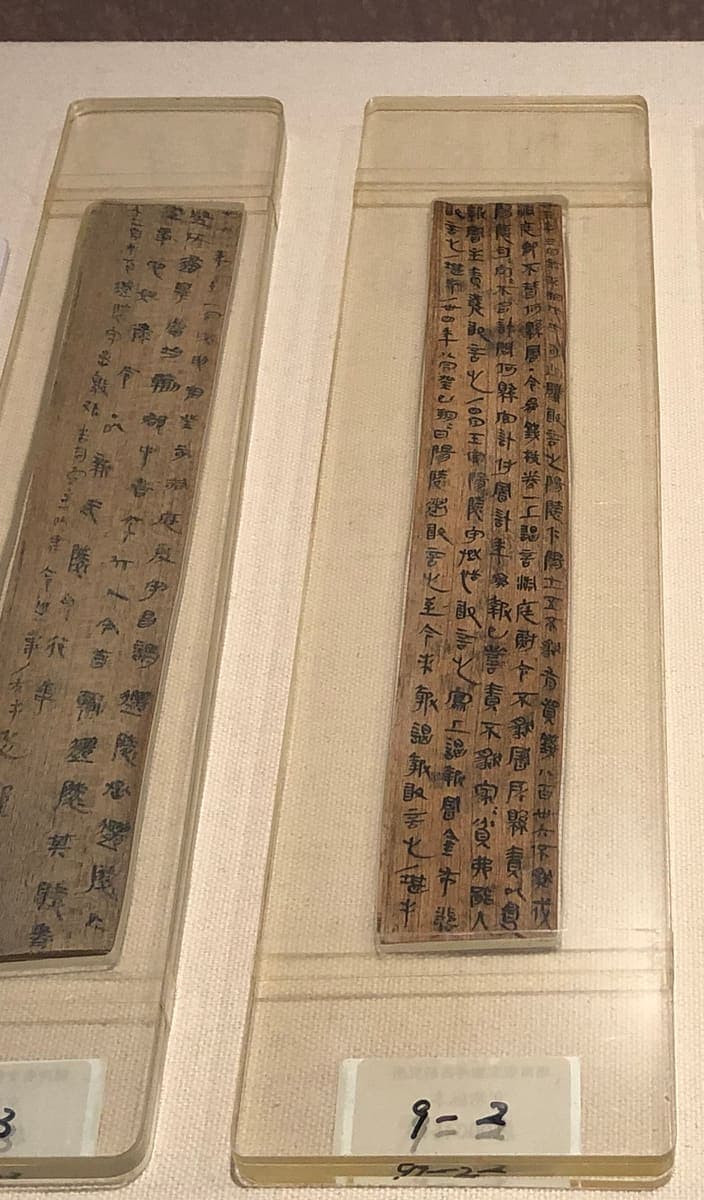 Two Qin wooden document boards in display mounts, each covered with several columns of small dark clerical-script characters