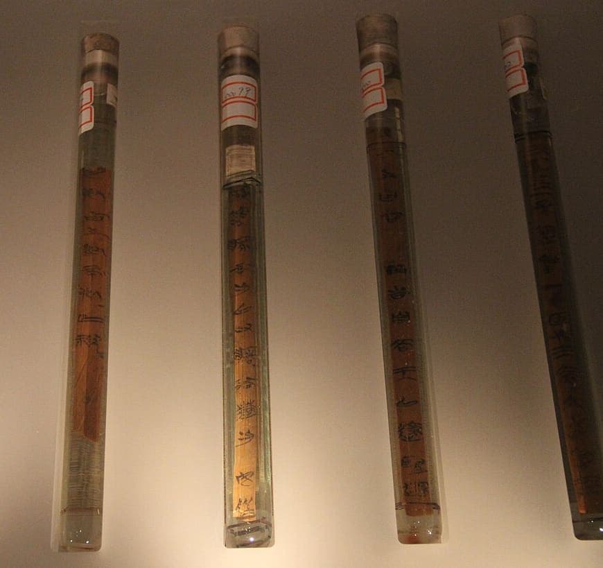 Four bamboo slips sealed upright in glass tubes of preservative, each with a numbered label on the cap and a column of ink graphs