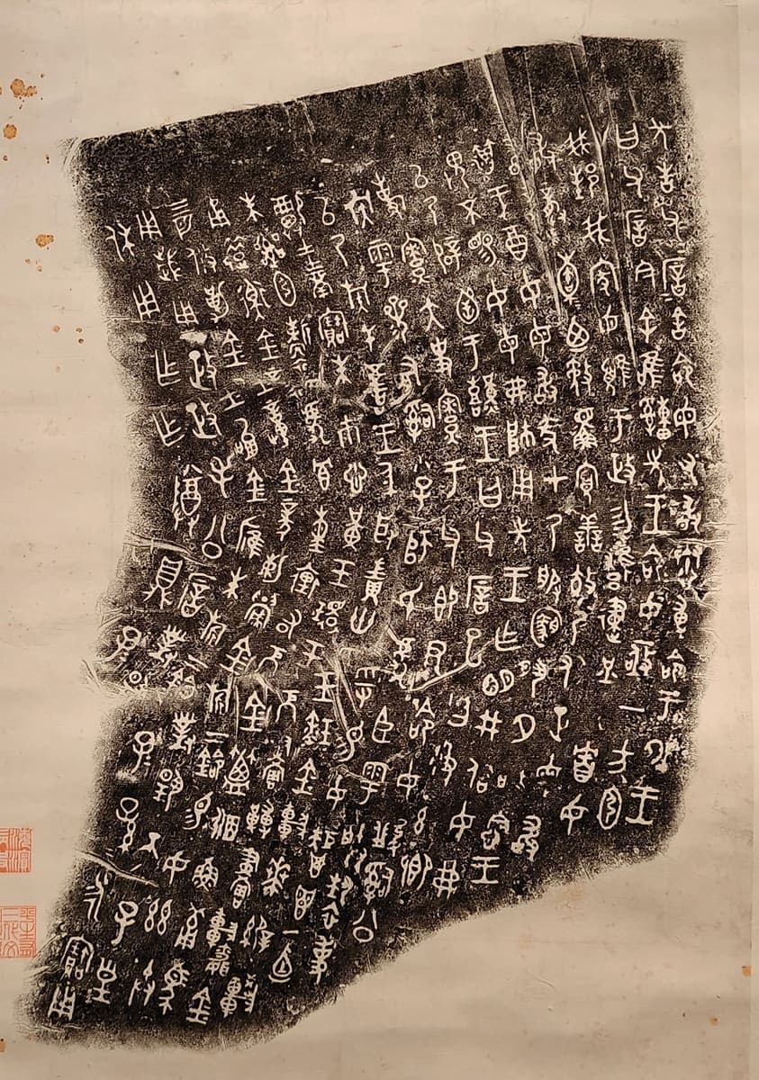 Qing hanging scroll mounting a rubbing of the Mao Gong ding inscription, white graphs on black with two red seals and foxing on the paper