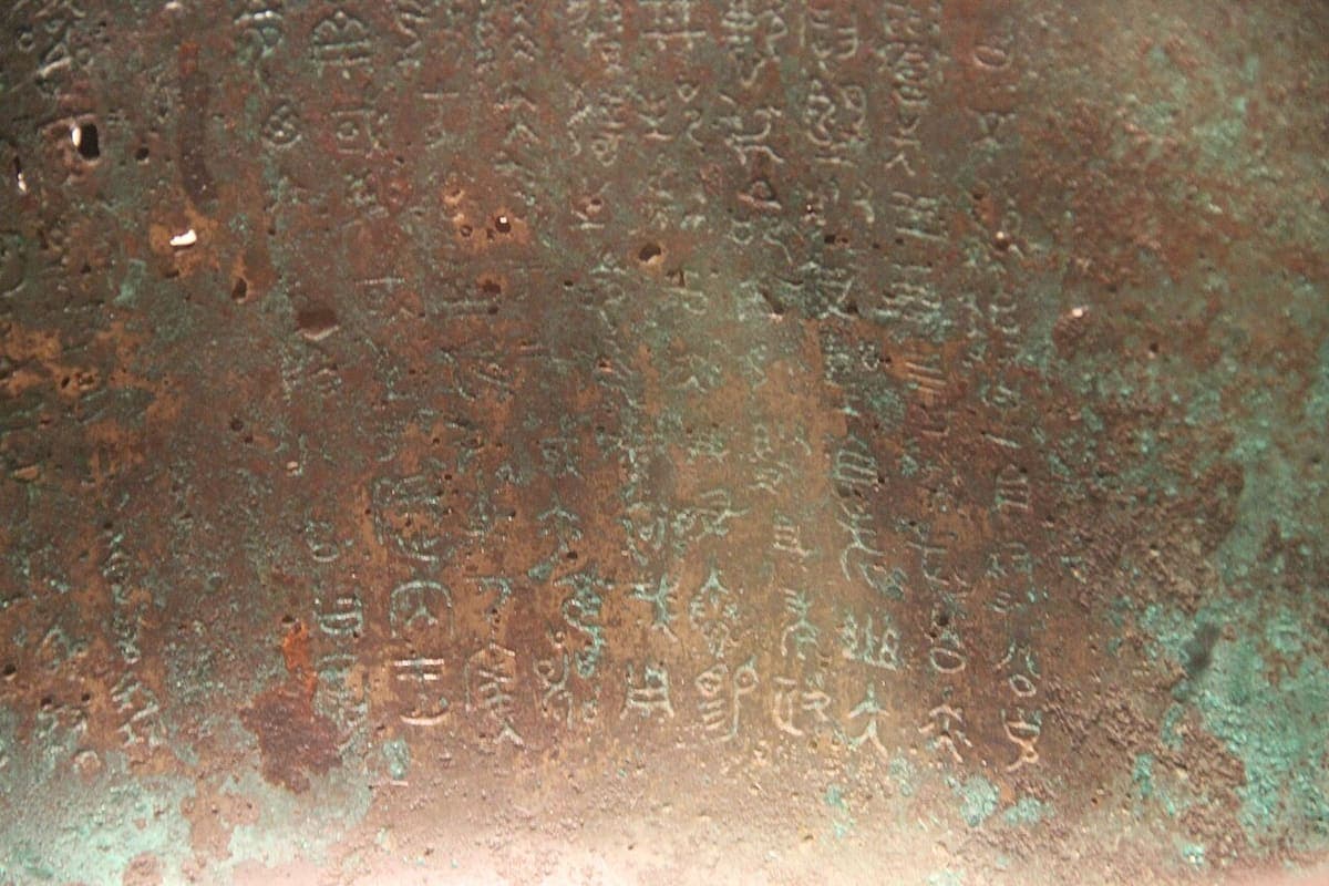 Close photograph of graphs cast into the green-patinated inner wall of a bronze cauldron, lit from one side