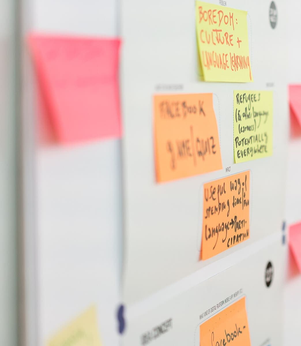 Orange, yellow and pink sticky notes arranged in a grid on a white workshop panel, the nearest notes blurred and only the middle band in focus
