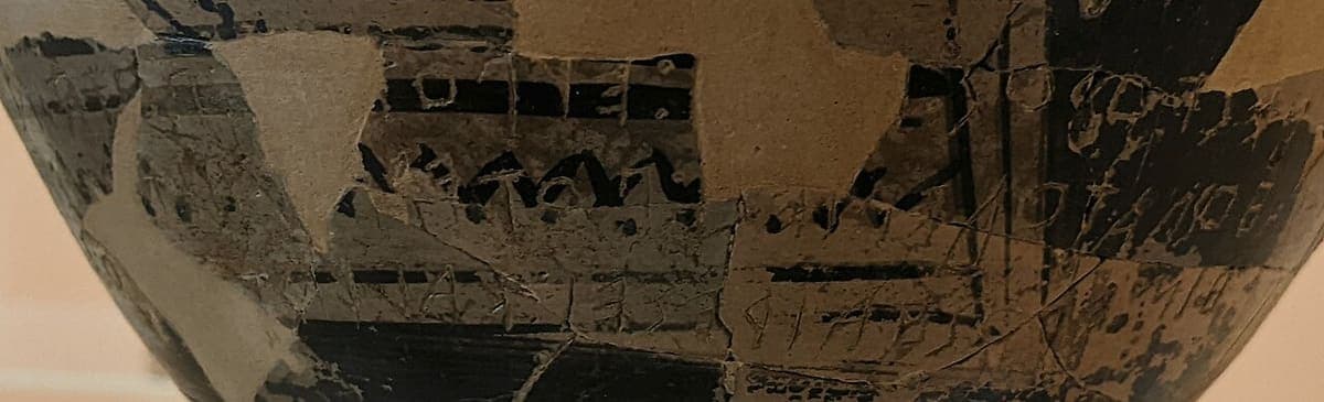 Detail of a small Geometric cup with faint right-to-left Greek letters scratched through the dark painted band and a repaired break running across it